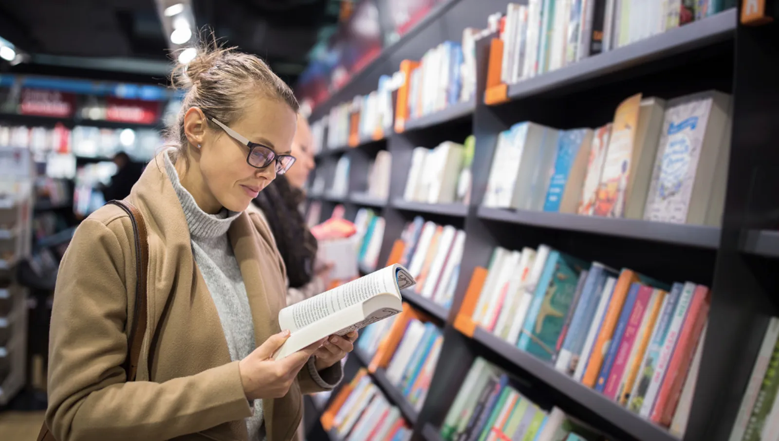 Person bläddrar i en bok framför en hylla med färgglada böcker i en modern bokhandel.
