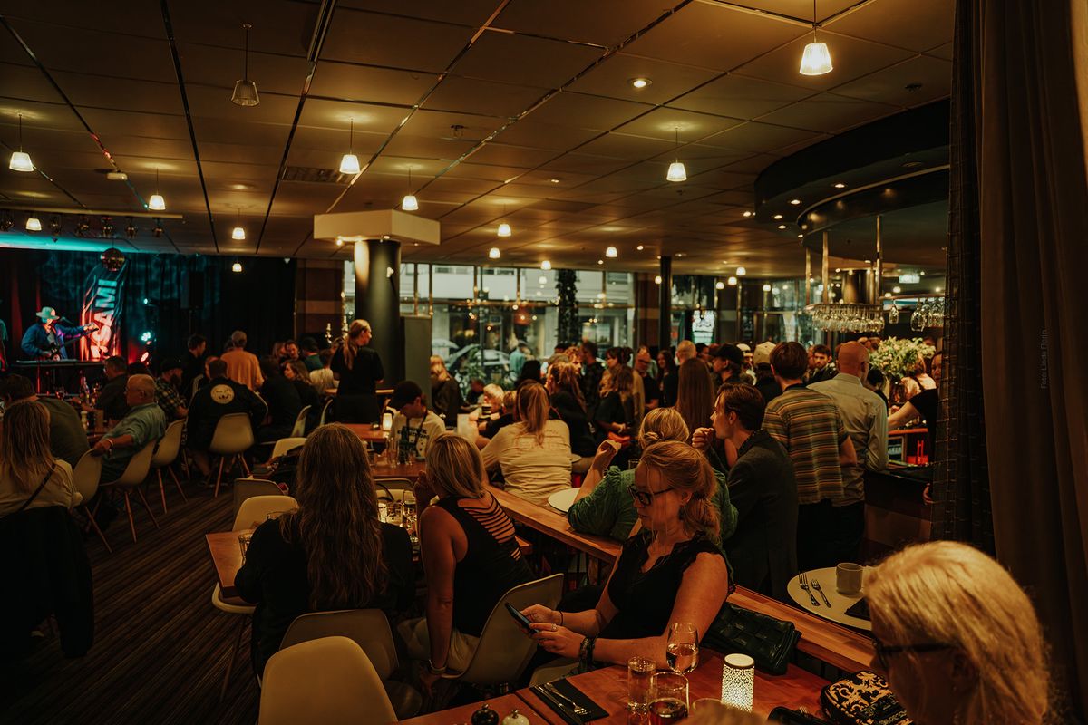 Stort öppen restauranglokal med scen till vänster och bar till höger fyllt av sittande gäster