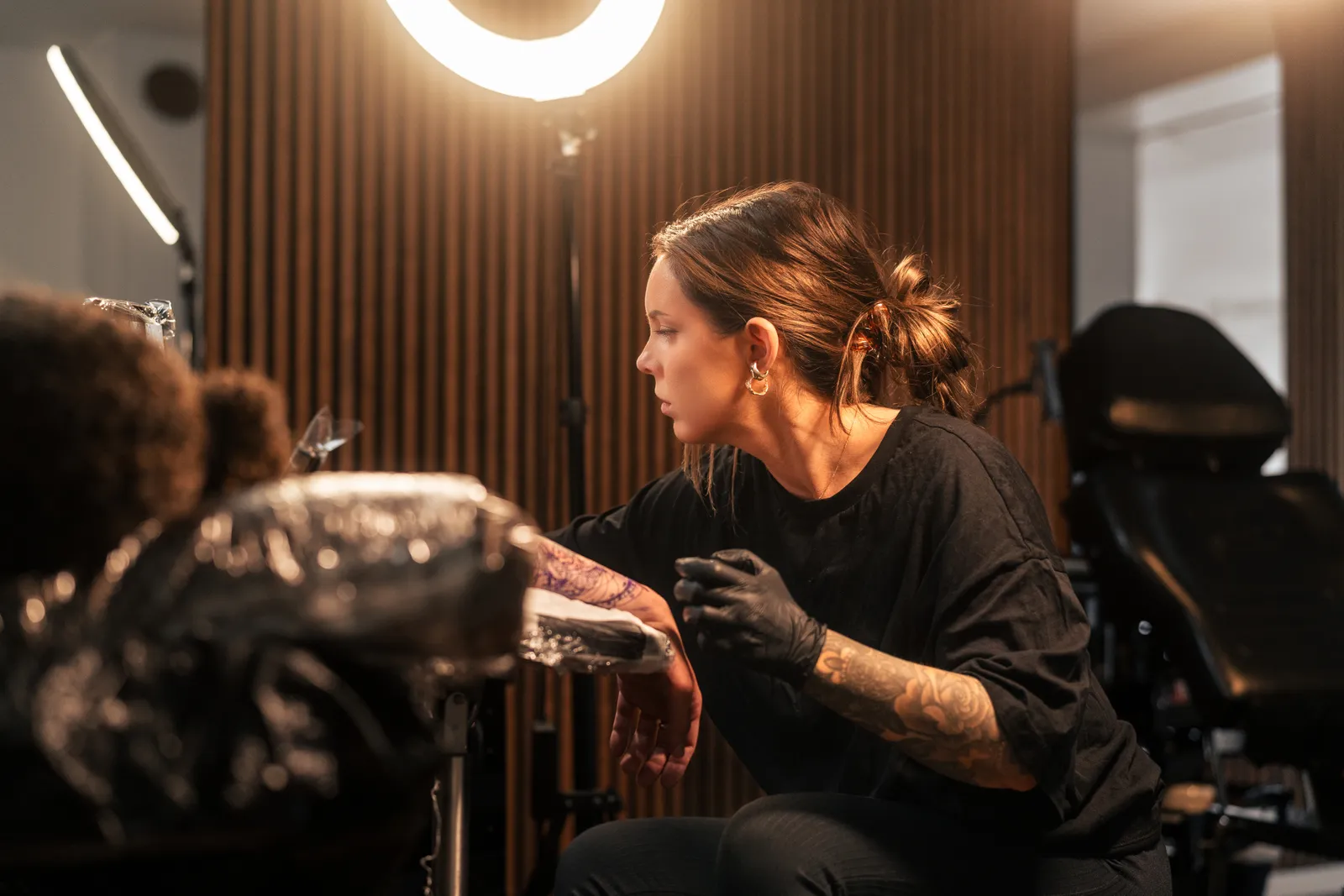 Tatuerare arbetar med en kunds arm i en tatueringsstudio med professionell belysning och utrustning.