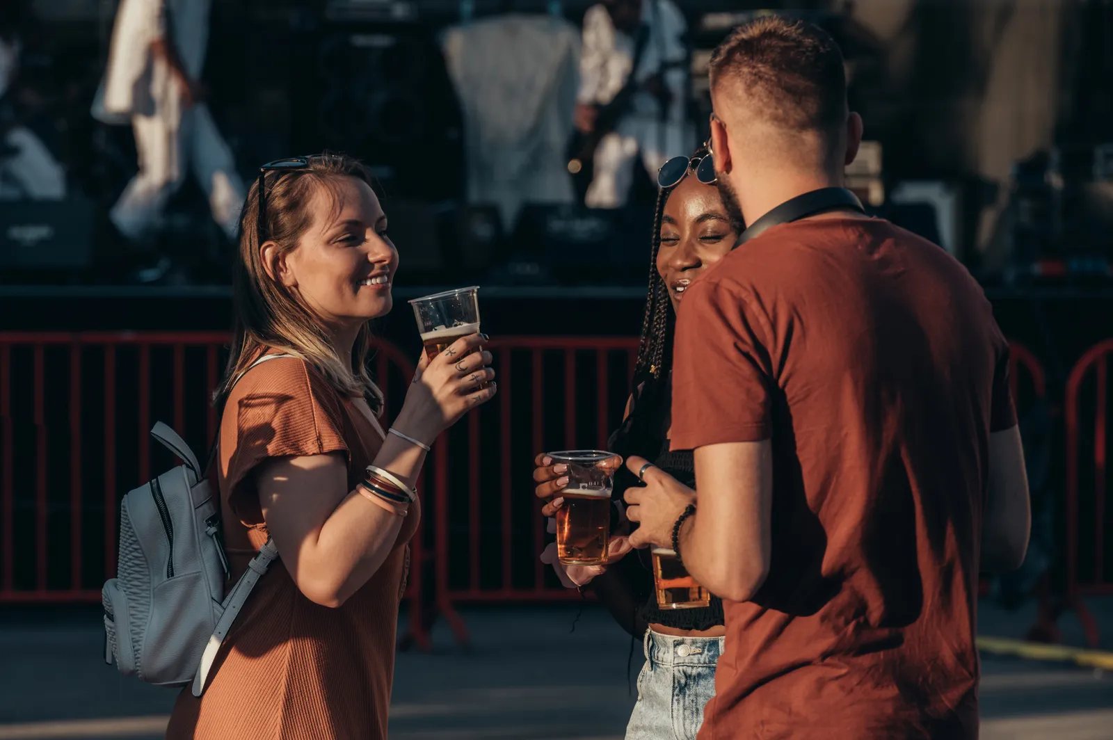 Personer står vid en utomhusbar och håller plastglas med öl under ett musik- eller festivalarrangemang.