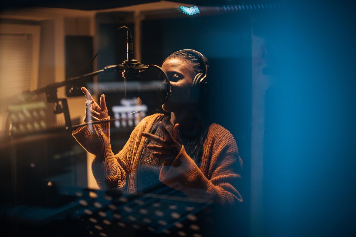 Kvinna står med hörlurar och sjunger in i en mikrofon i musikstudio